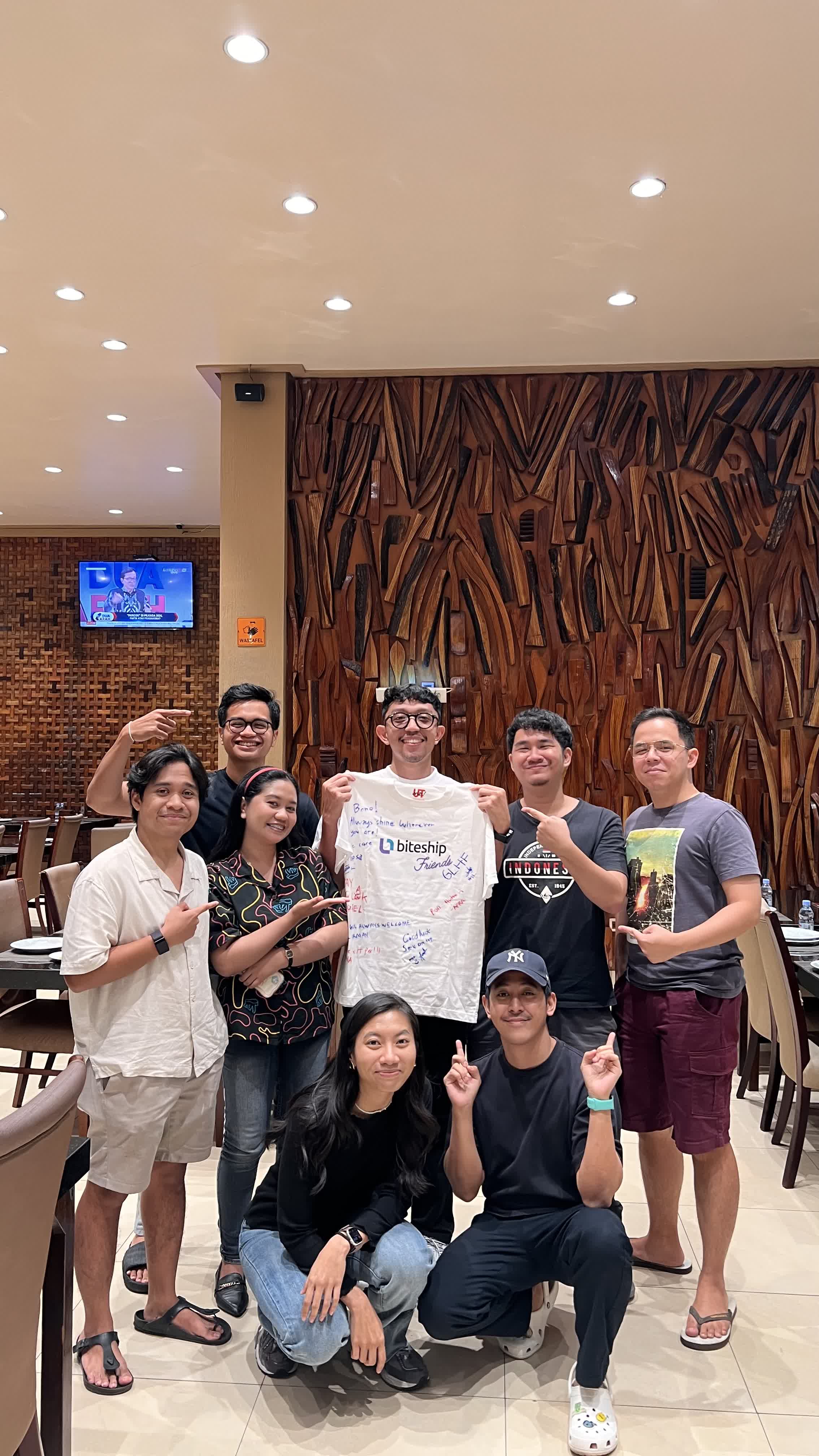 Coworkers holding a signed Biteship shirt at a restaurant