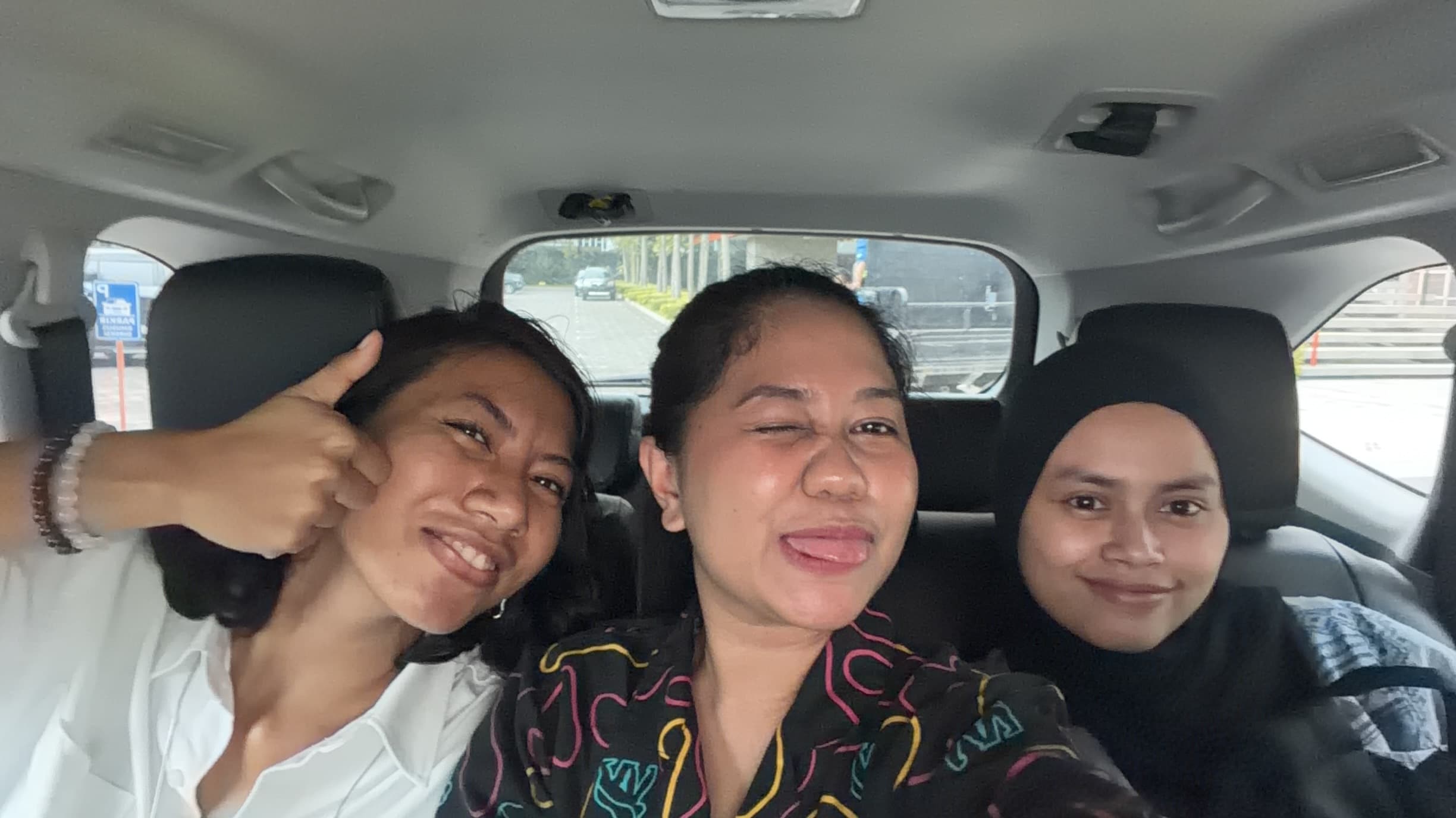 Three friends smiling together in a car selfie